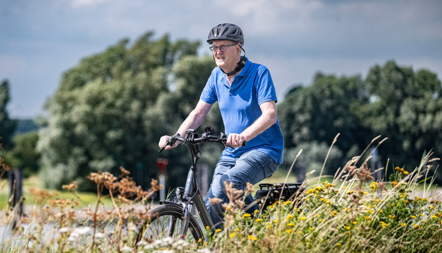 Oude man op de elektrische fiets in de natuur, want is fietsen op de elektrische fiets gezond?